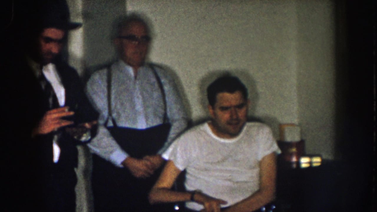 A man in a hat holds a glass while another man stands behind a seated wheelchair user.