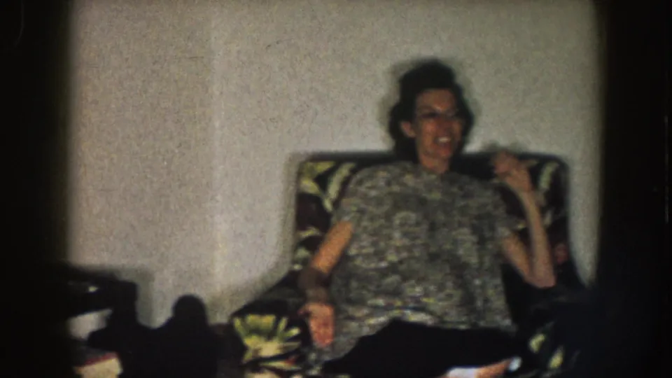 1957 Nebraska frame showing a woman leaning back in a floral armchair as the home-movie camera pans.