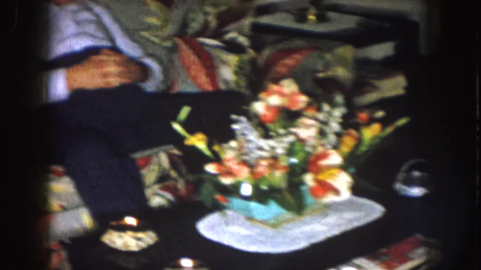 1957 Nebraska living room detail showing a flower arrangement on a table with seated men partly visible behind it.