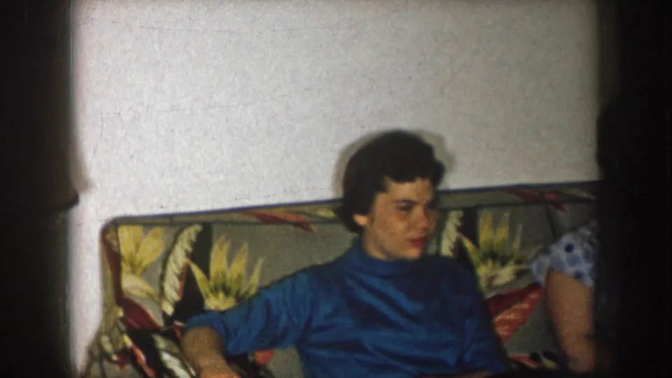 The seated woman in a blue turtleneck turns toward someone just outside the frame in a 1957 Nebraska interior.