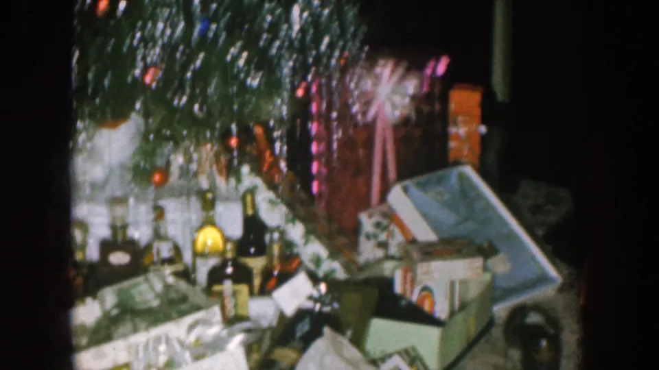 Nebraska 1957 home-movie view of open gift boxes, loose wrapping paper, bottles, ornaments, and tinsel near the tree.
