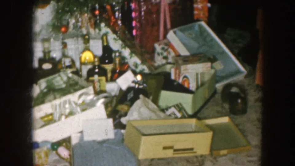 Nebraska 1957 frame showing scattered packages, bottles, loose paper, a gift box, and tree ornaments after a holiday gathering.