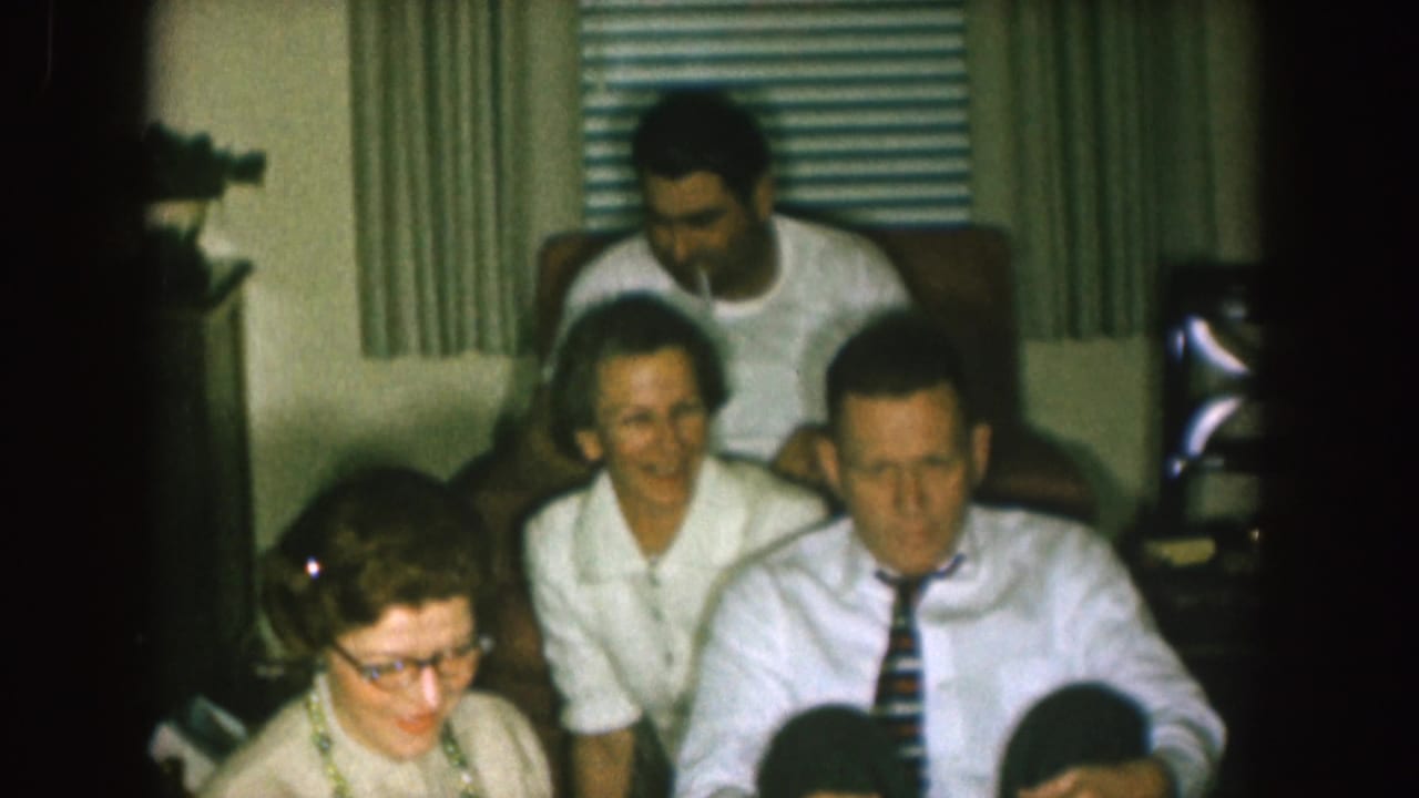 Adults gathered on living room seating with blinds and curtains behind them.