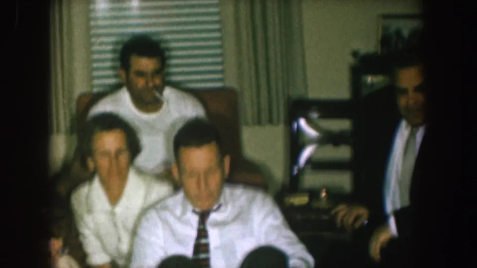 1957 Nebraska home-movie frame of a family group seated in a private living room with a television nearby.