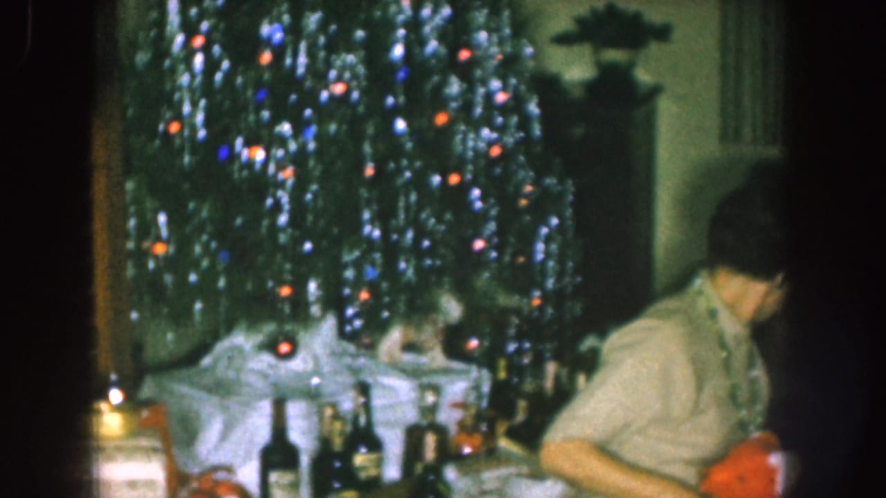 Decorated Christmas tree with lights beside adults gathered around a table indoors.