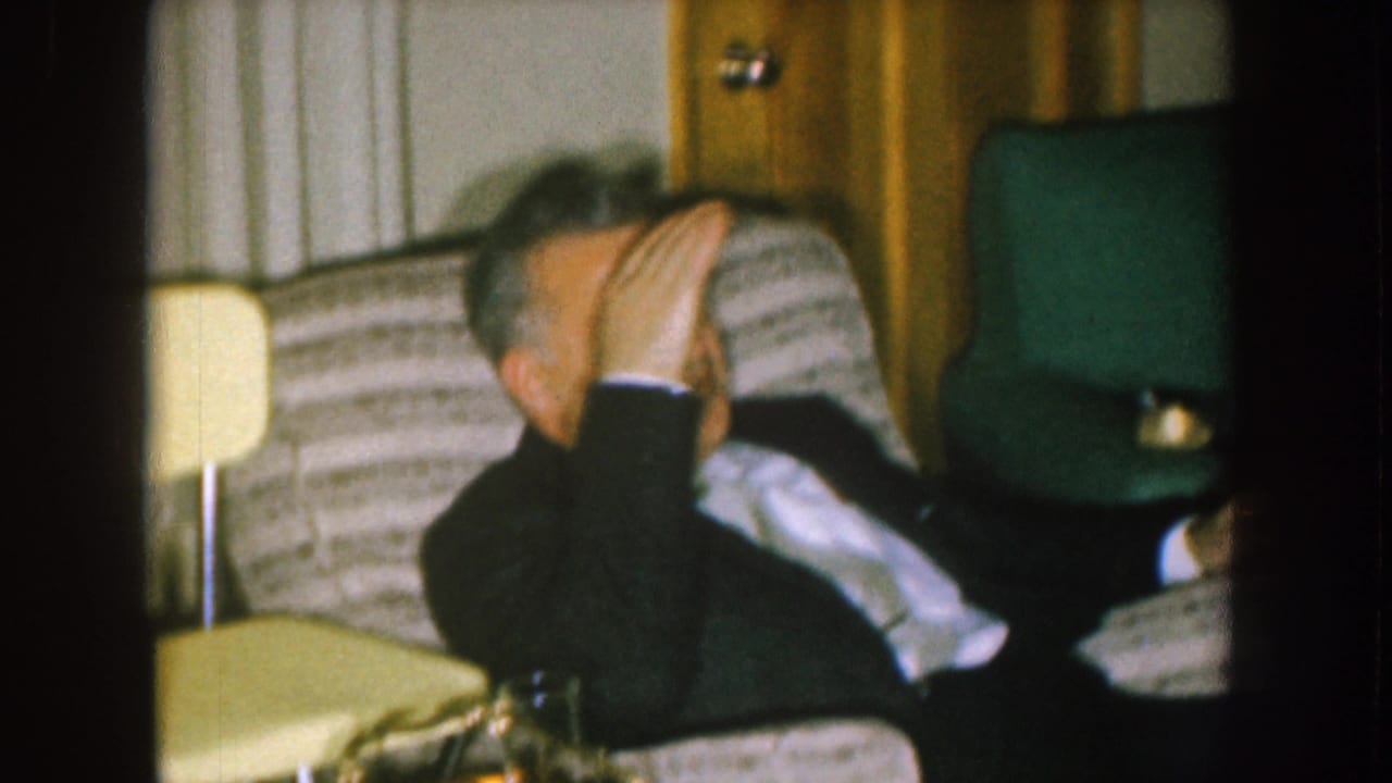 Seated man raises his hand toward his face in a living room chair.