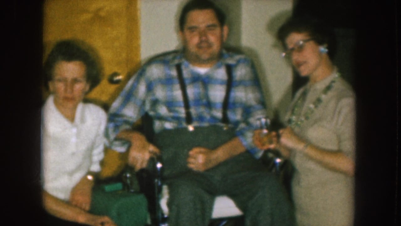 Three adults indoors, with a man in a wheelchair between two women.