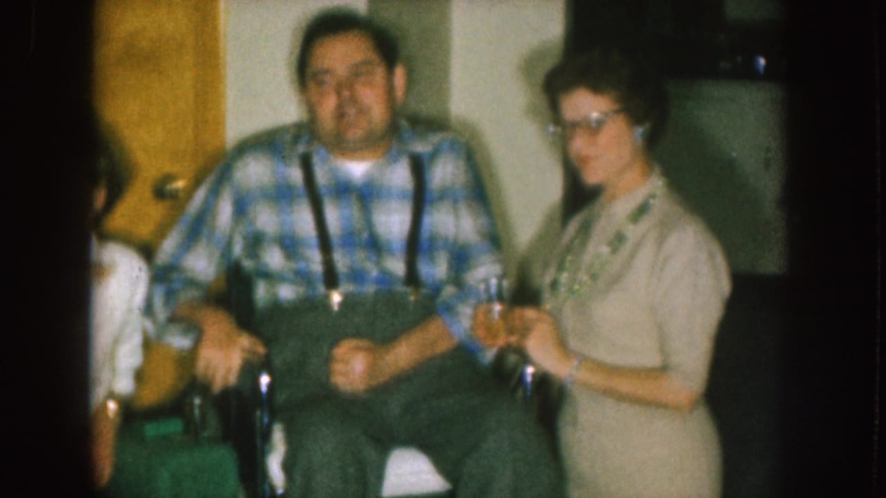 Man in wheelchair and woman in light dress pose near a doorway indoors.