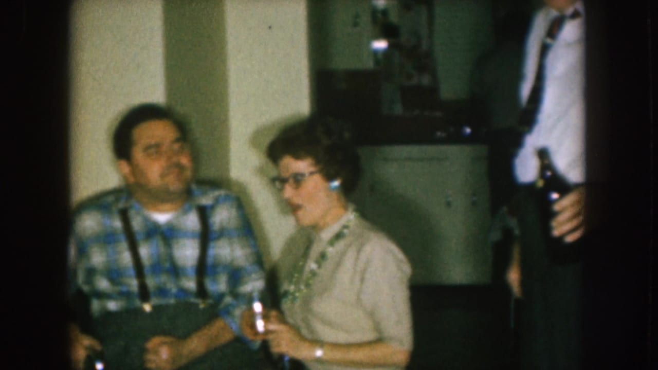 Seated man and woman talk while another adult stands nearby holding a bottle.