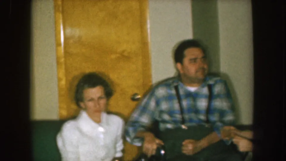 1957 Nebraska home interior showing a woman in a white top and a man in plaid seated near green upholstery and a yellow door.