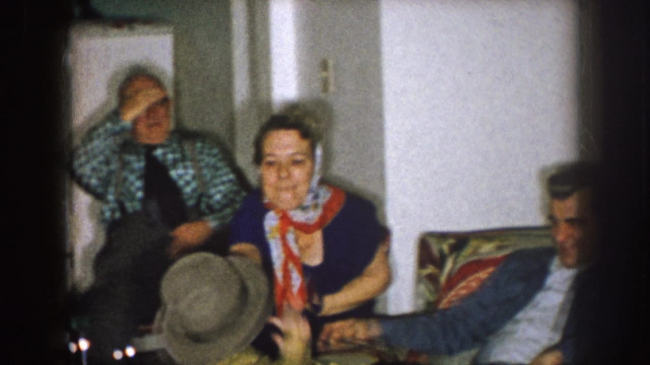Adults sit and talk in a home interior, with a woman in a red scarf near the center.
