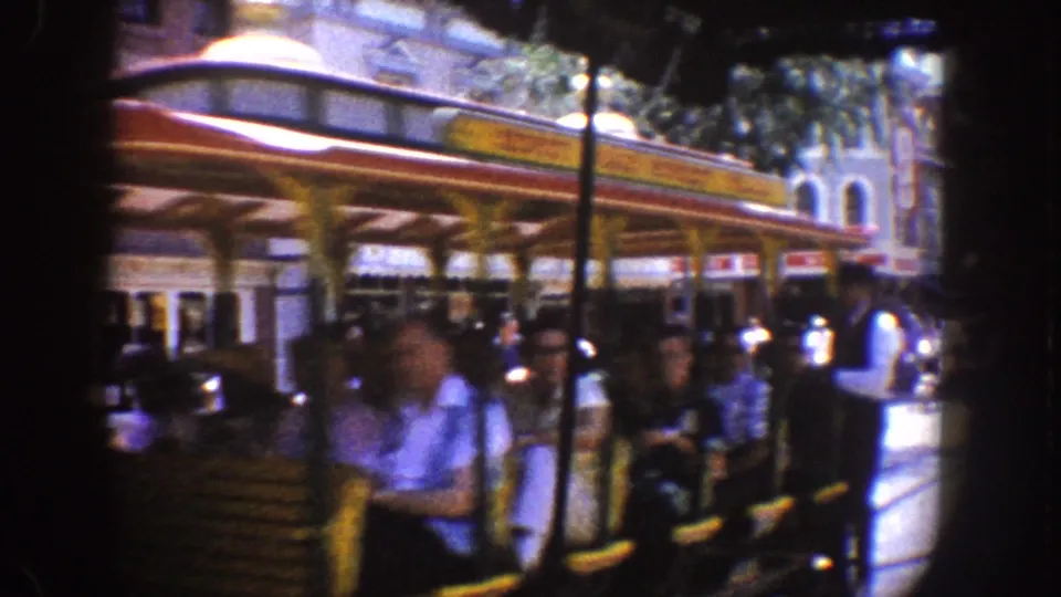 Passengers ride an open horse-drawn trolley at Disneyland, with staff and visitors visible near storefront facades.