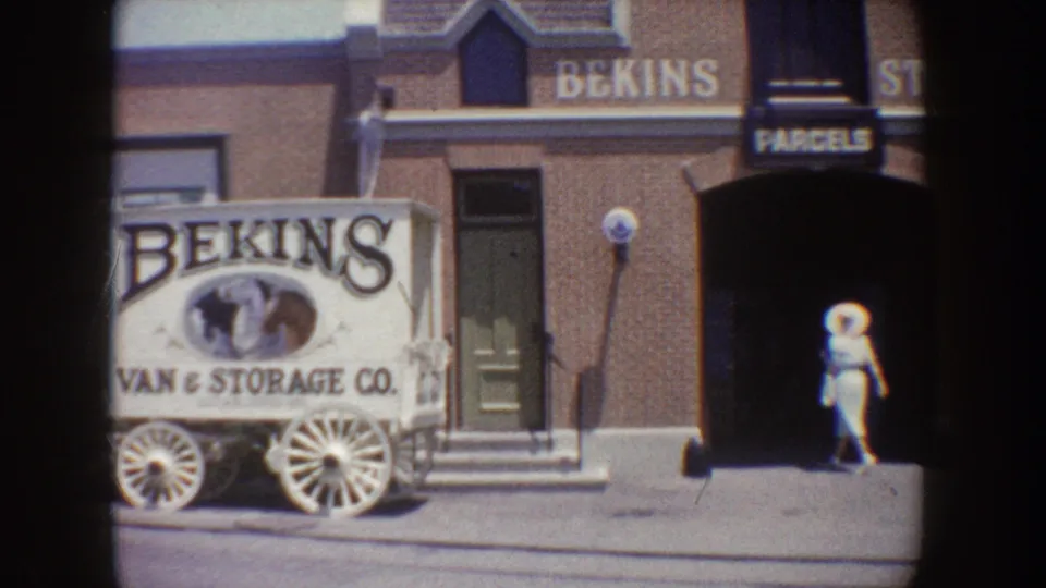 1962 Disneyland frame with a Bekins Van & Storage Co. delivery wagon display near storefront signs and a passing visitor.