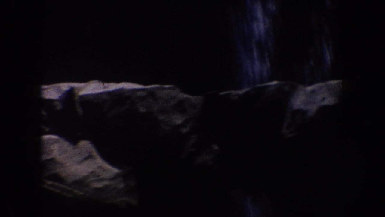 1962 Disneyland home-movie frame showing a dark rocky ride tunnel with artificial stone surfaces and limited detail in shadow.