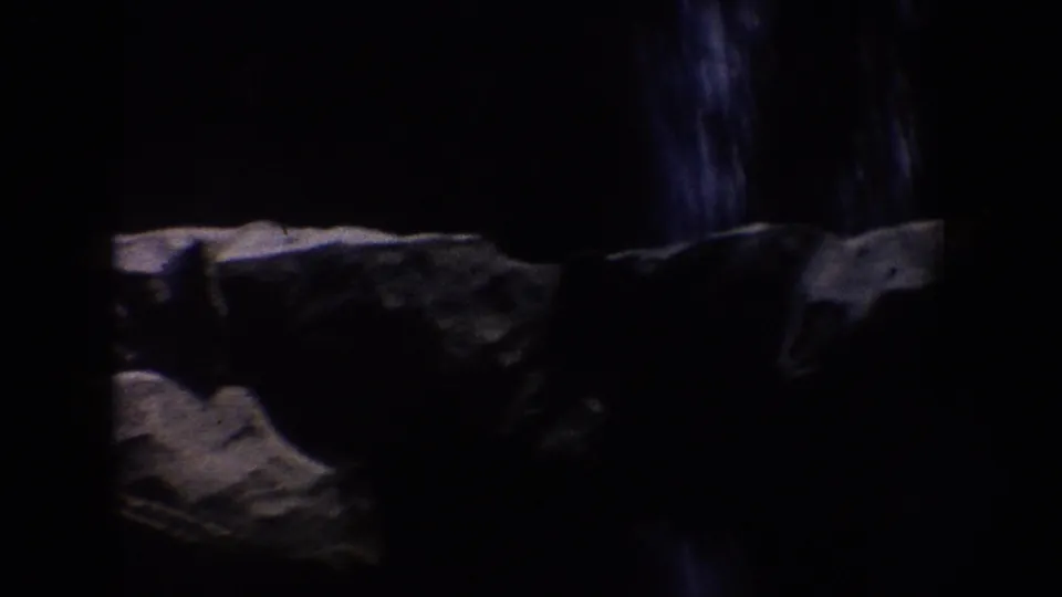 1962 Disneyland home-movie frame showing a dark rocky ride tunnel with artificial stone surfaces and limited detail in shadow.