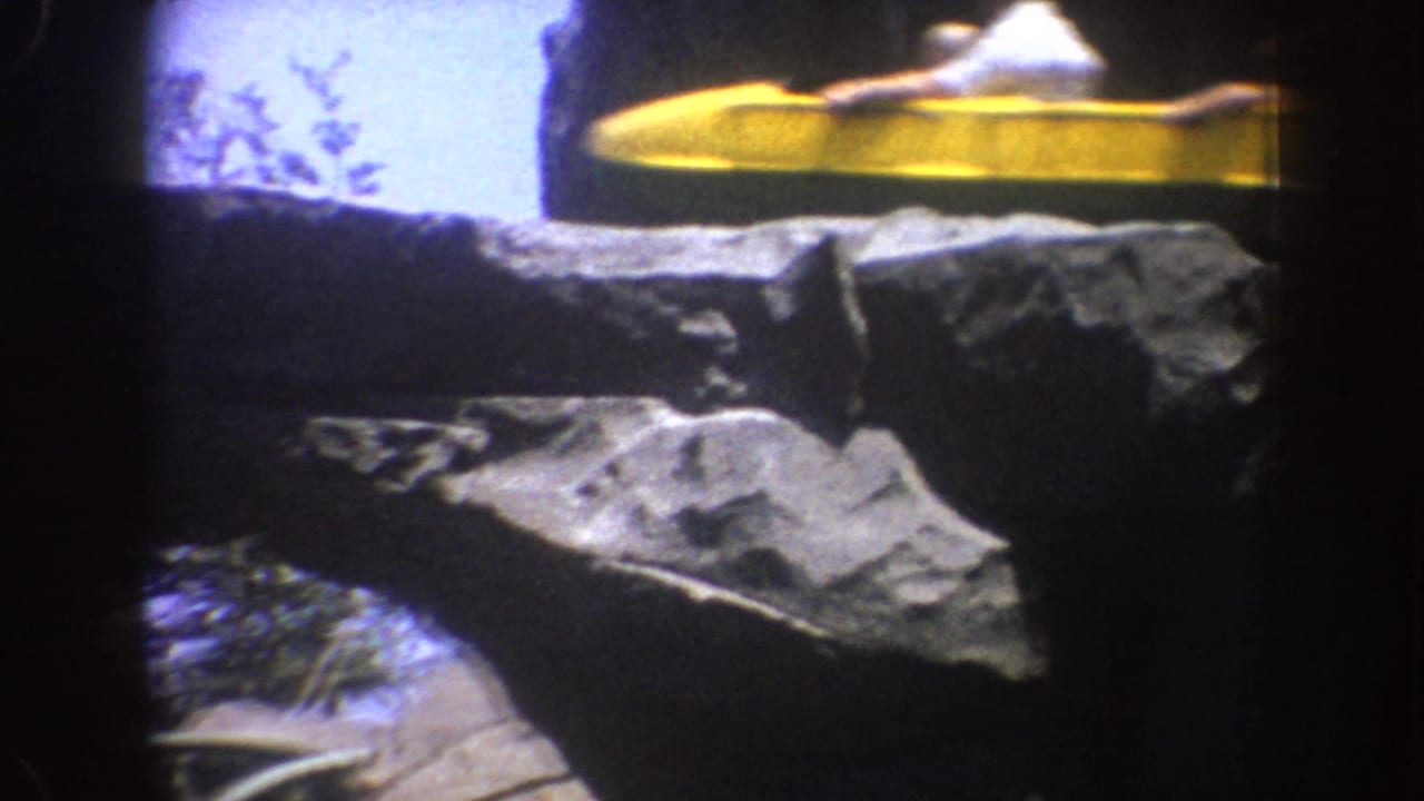 Yellow coaster train passes above gray rockwork near a bright sky opening.
