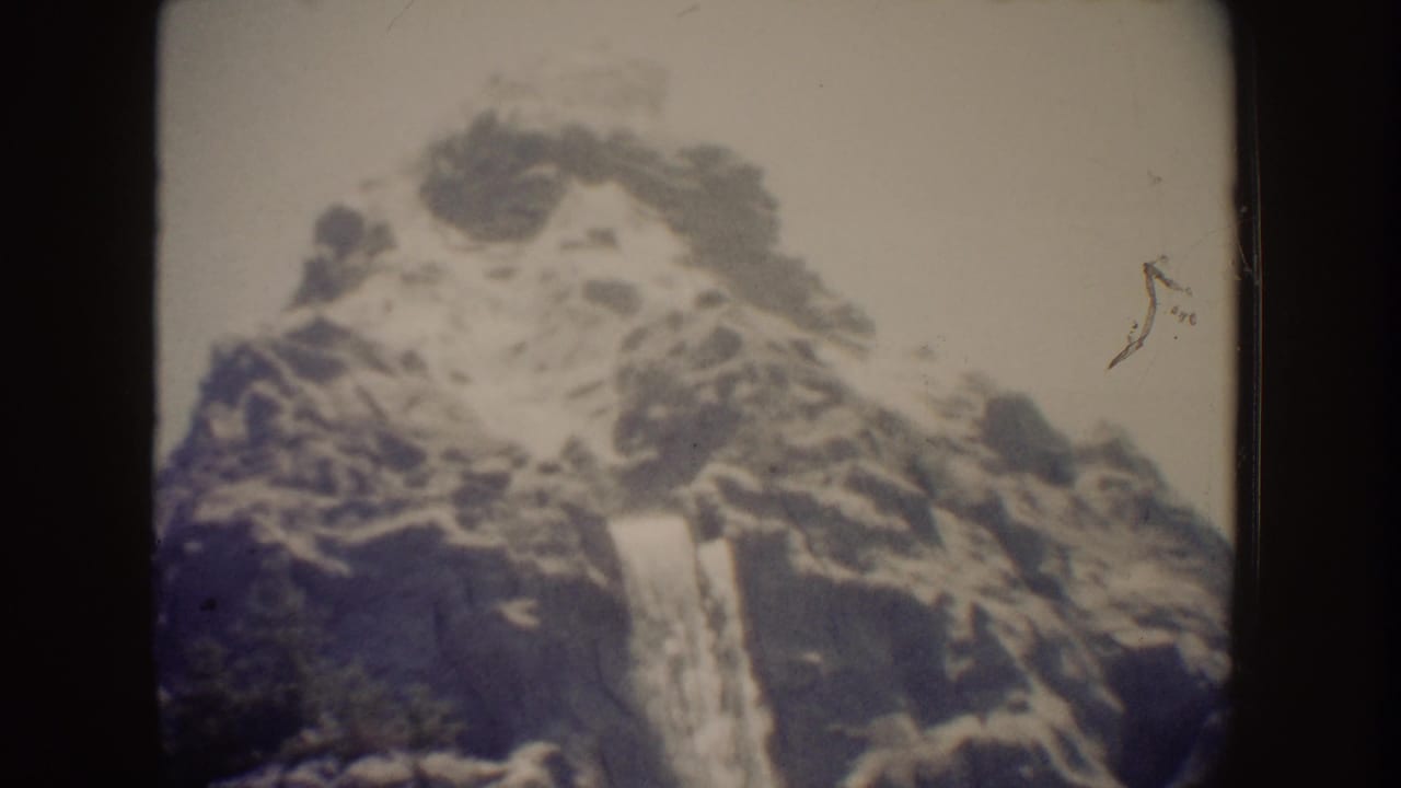 1962 Disneyland home-movie frame showing a waterfall spilling over a rocky cliff face with soft focus and faded color.