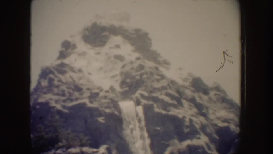 1962 Disneyland home-movie frame showing a waterfall spilling over a rocky cliff face with soft focus and faded color.
