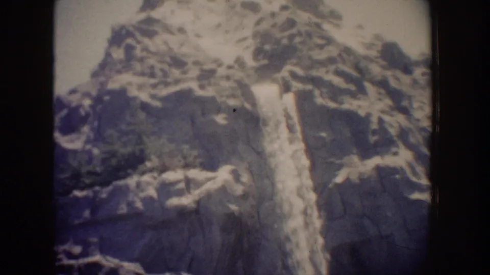 Visitor-shot 8mm view of a Disneyland waterfall running down a steep rock wall, bordered by the scanned film frame.