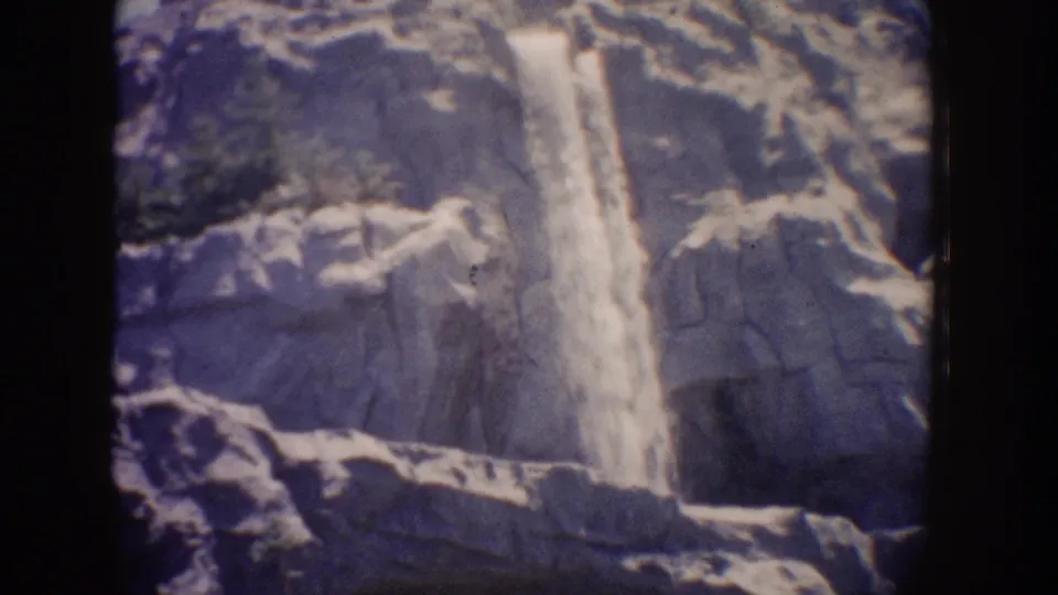 1962 8mm frame showing water cascading past layered rock ledges at Disneyland, with blue-toned fading and grain.