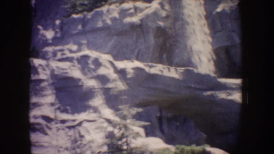Home-movie frame of the lower rocky waterfall area at Disneyland, with soft exposure, grain, and dark film edges.