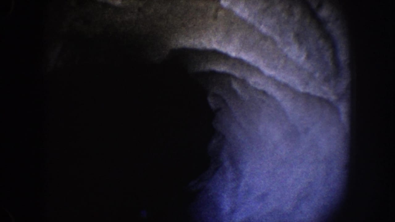1962 Disneyland home-movie frame showing a blue-purple illuminated cave-like surface surrounded by deep darkness.