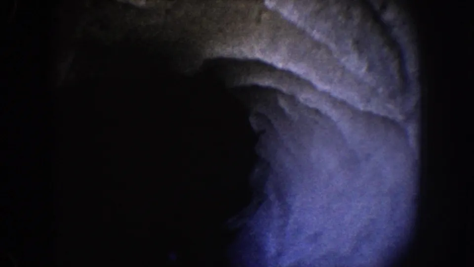 1962 Disneyland home-movie frame showing a blue-purple illuminated cave-like surface surrounded by deep darkness.