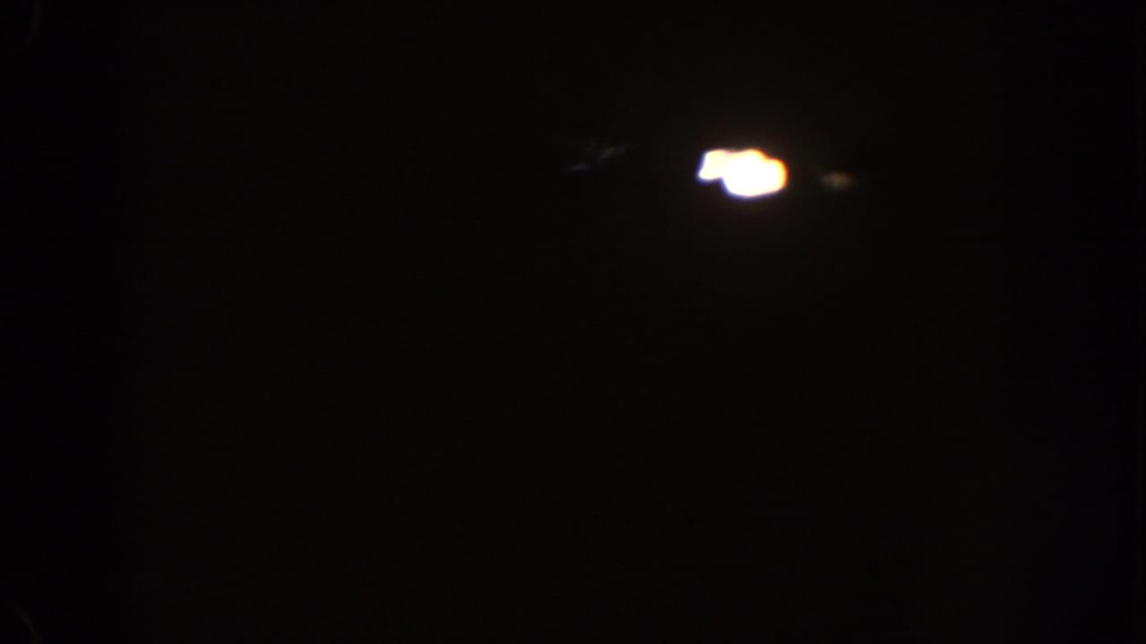 Very dark 1962 Disneyland 8mm frame with small blooming lights and little visible detail beyond shadow.