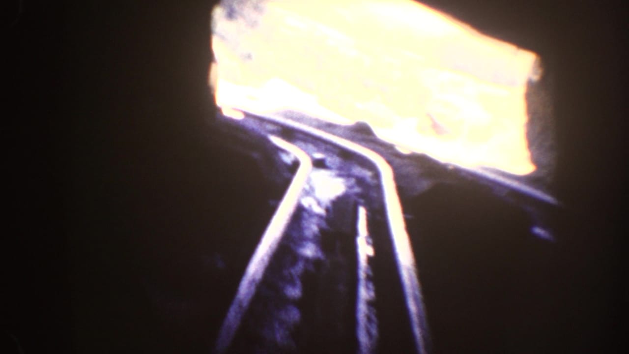 1962 Disneyland home-movie frame from inside a dark train tunnel, with tracks curving toward daylight.