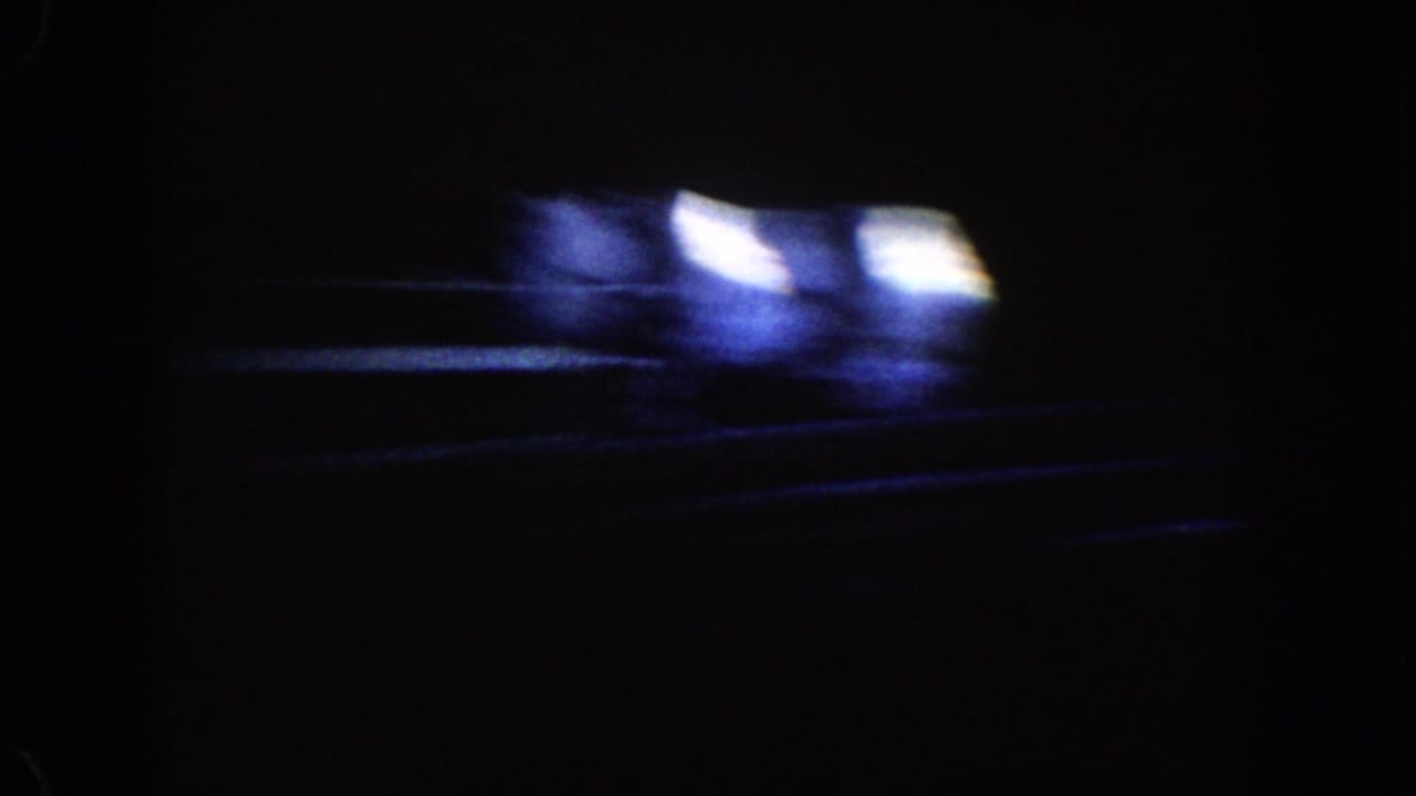 1962 Disneyland ride footage begins in near darkness, with blurred blue-white lights and faint track-like lines across the frame.