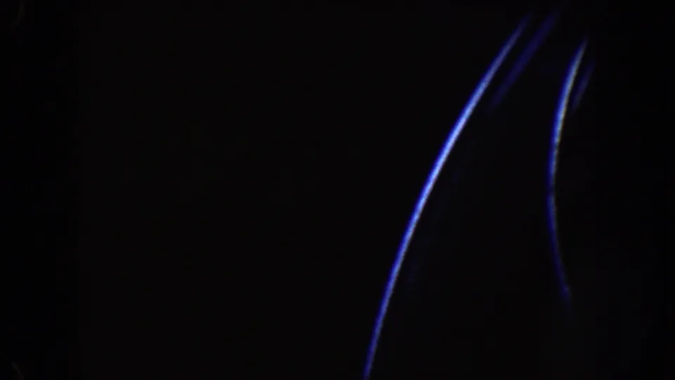 Dark 8mm frame from the Disneyland ride, showing curved blue light streaks at the right edge and little visible detail elsewhere.