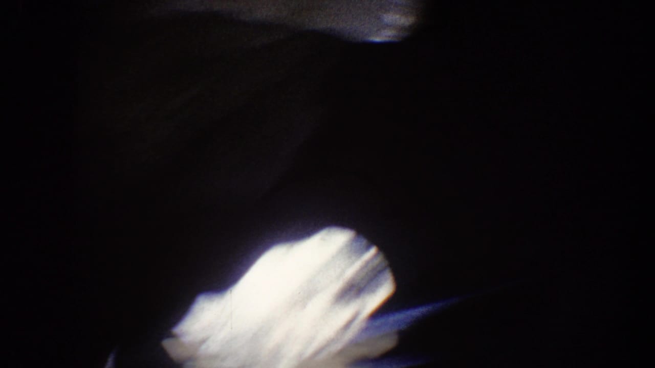 1962 Disneyland home-movie frame showing a dark passage with a bright white blur and indistinct shadowed forms.