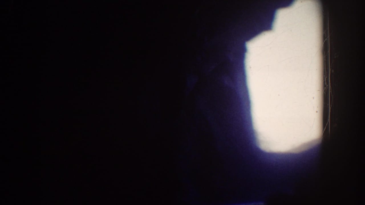 Dark, heavily underexposed 8mm frame from the Disneyland ride clip, with a bright blown-out patch and little readable detail.