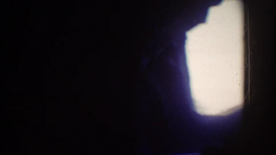 Dark, heavily underexposed 8mm frame from the Disneyland ride clip, with a bright blown-out patch and little readable detail.