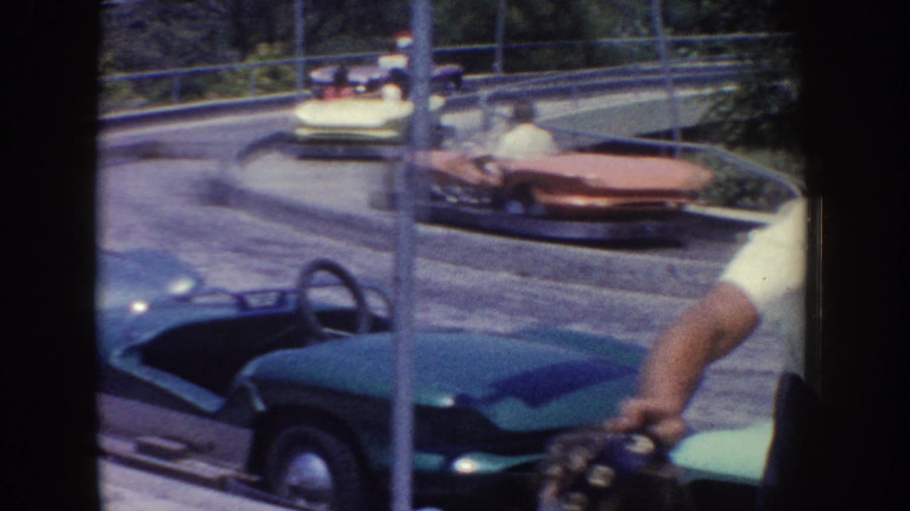 1962 Disneyland home-movie frame showing green, red, and yellow ride cars moving along a curved track with visitors aboard.