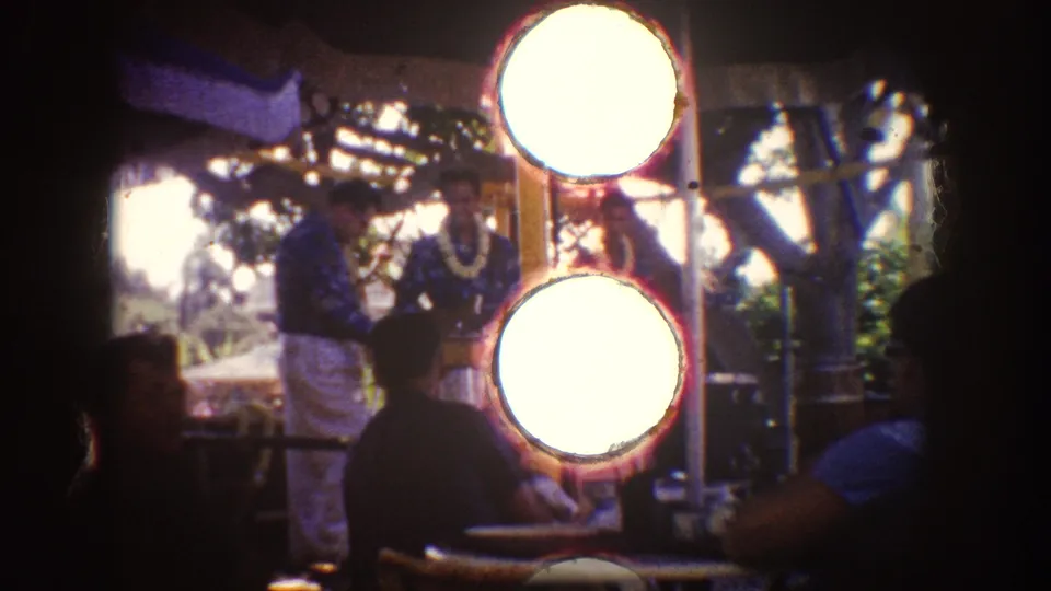1962 Disneyland frame with Hawaiian-style performers and seated visitors partly obscured by bright circular flare from the film scan.