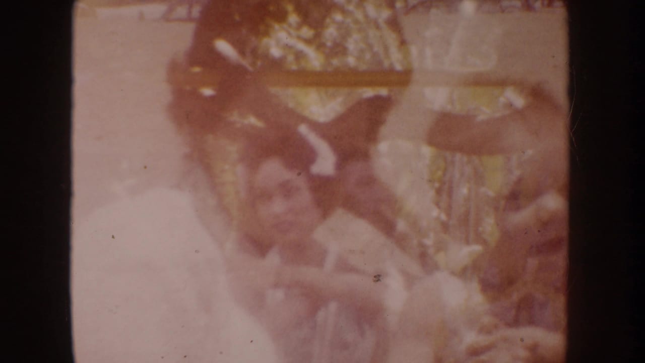 1962 Disneyland home-movie frame showing a woman in white leaning toward a baby, softened by faded color and film grain.