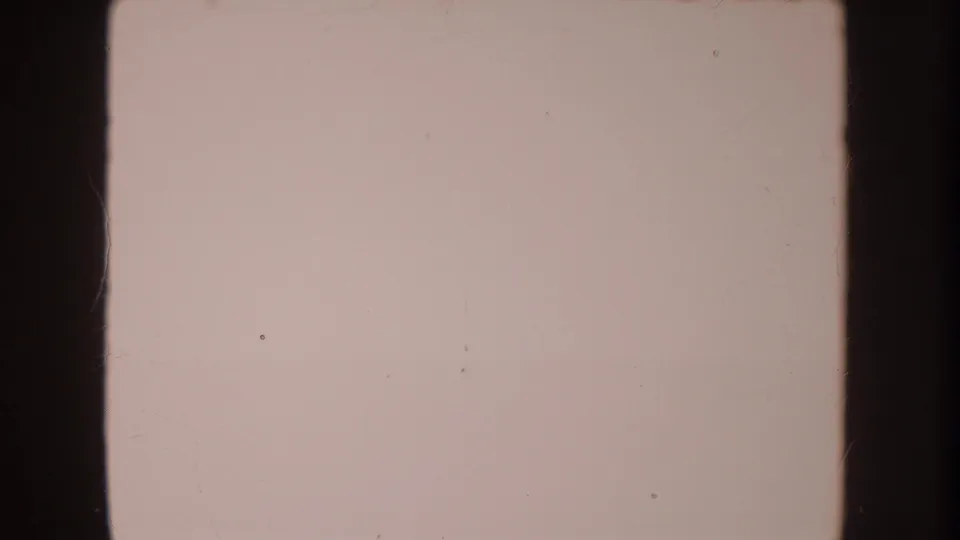 Soft, faded 8mm frame from the 1962 Disneyland home-movie clip, showing a pale blanket or surface with dark film borders and visible dust.