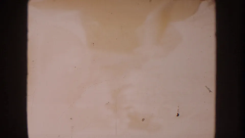 Faded 8mm frame from the 1962 Disneyland home-movie clip, with a baby in light clothing partially visible on a pale blanket.