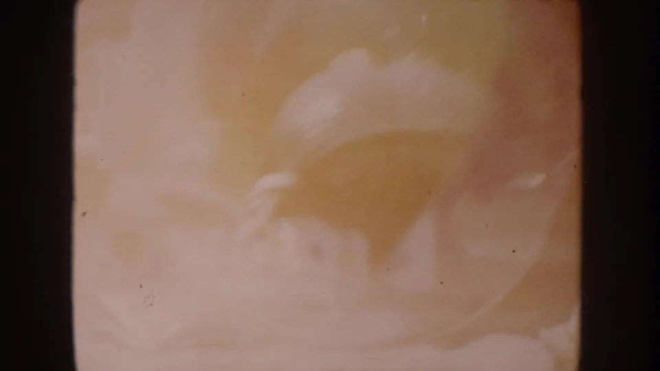 Warm soft-focus 8mm frame from the 1962 Disneyland clip with pale rounded forms and amber color drift.