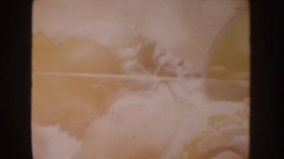 Very soft 1962 home-movie frame with a pale blanket area and indistinct infant-like form in warm faded color.