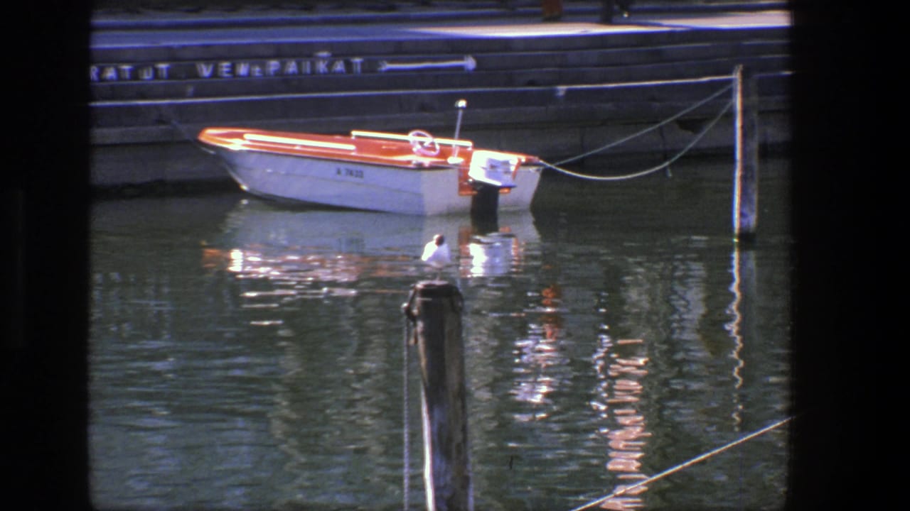 Small white and orange motorboat moored by a stone quay with a gull on a post in the foreground.