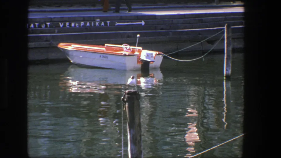 1975 Denmark 8mm view of a moored leisure boat near a stone quay, with reflected orange trim and a gull perched in front.