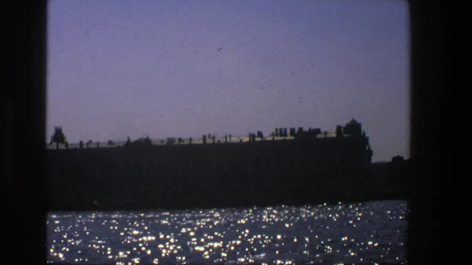 1975 Denmark 8mm frame showing a silhouetted waterfront building against a twilight sky with bright reflections across the water.
