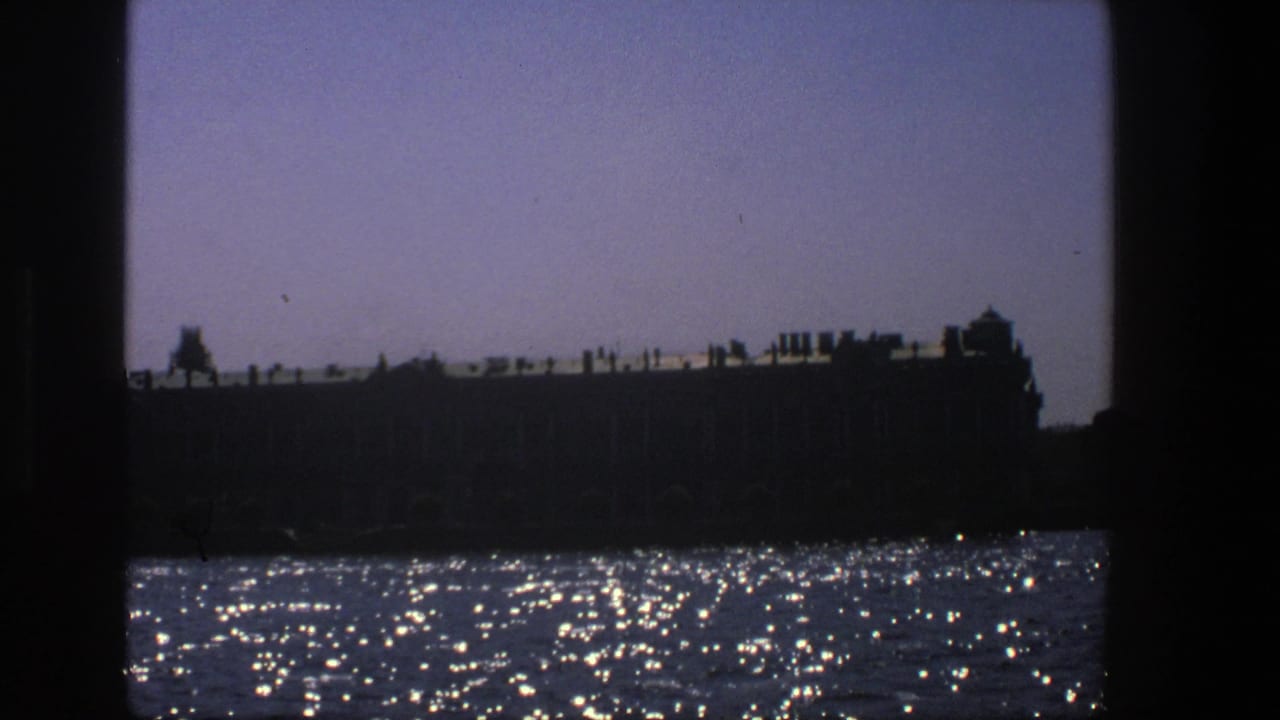 1975 Denmark 8mm frame showing a dark historic-looking waterfront structure above bright, glittering water.