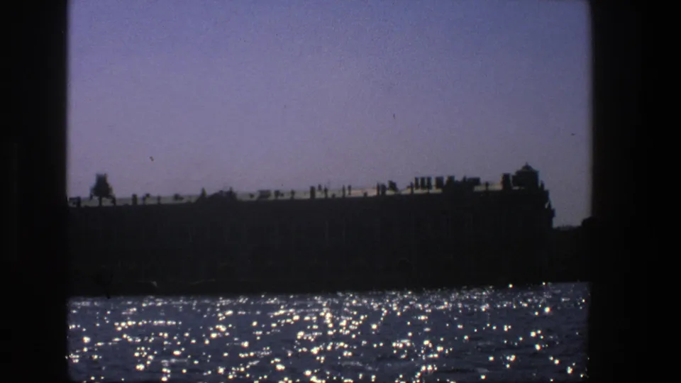 1975 Denmark 8mm frame showing a dark historic-looking waterfront structure above bright, glittering water.