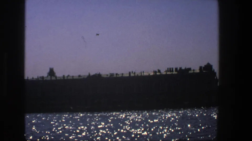 1975 Denmark 8mm view of a long silhouetted structure across shimmering water, with heavy dark borders.