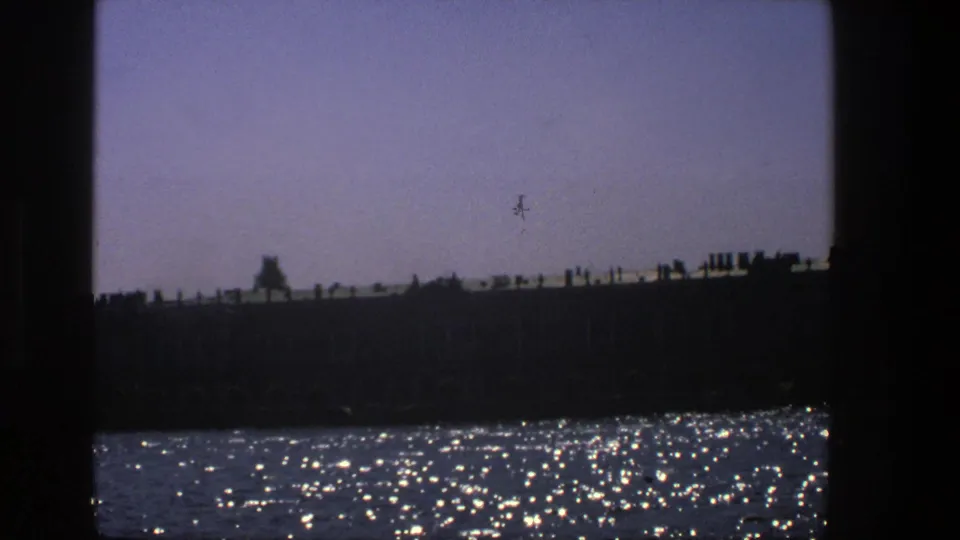 Denmark 1975 home-movie frame with rippling water in the foreground and a silhouetted waterfront structure beyond.