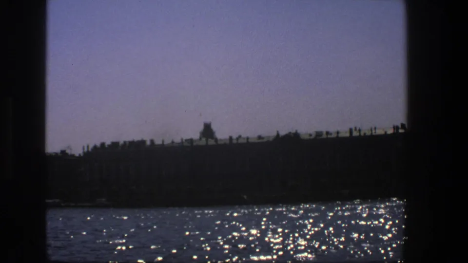 The boat-level view holds on a dark Danish riverside outline with glittering water reflections and a hazy sky.