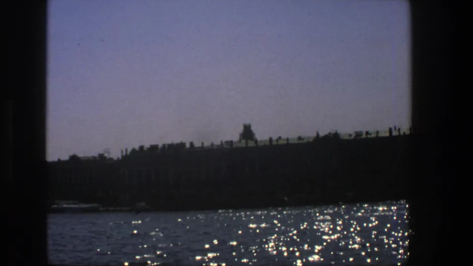 A muted 8mm frame shows the riverside silhouette lower in view, with bright ripples and dark borders suggesting a boat window.